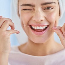 Woman squinting as she flosses her teeth