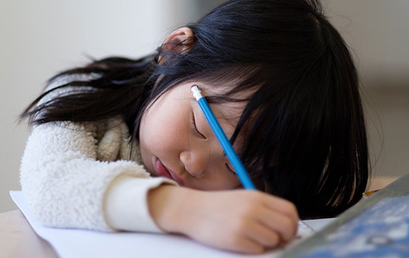 Exhausted girl with children’s sleep apnea sitting at desk