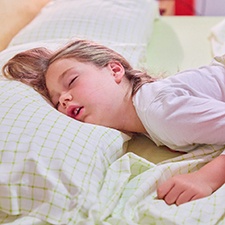 Snoring little girl in bed with green sheets