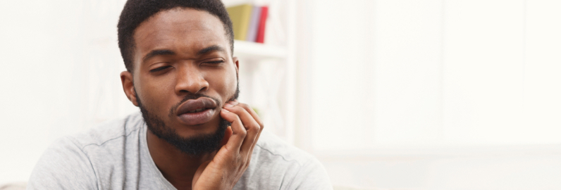 Man in need of emergency dentistry holding cheek in pain