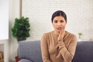 Worried woman sitting on couch and rubbing her jaw